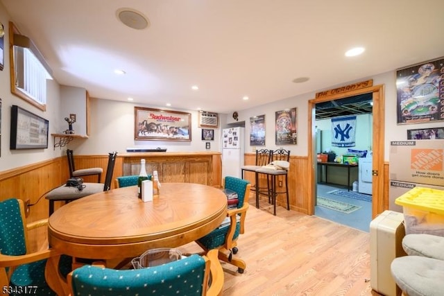 dining space with light wood finished floors, recessed lighting, wainscoting, and wood walls