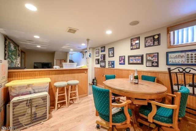 dining space with recessed lighting, a bar, wood finished floors, and wainscoting