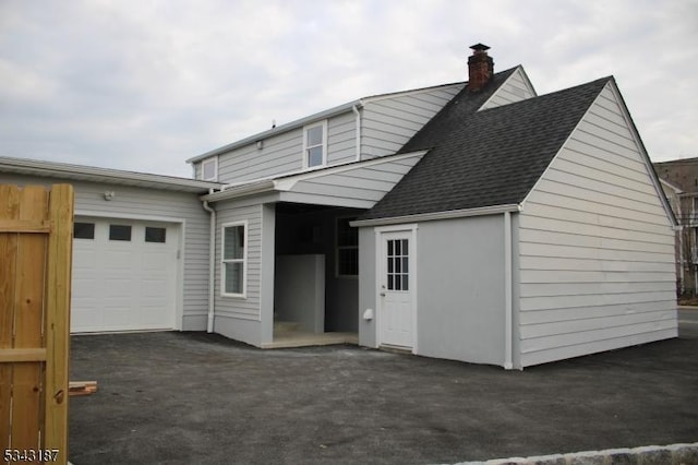 rear view of property with aphalt driveway, a garage, roof with shingles, and a chimney