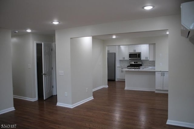 kitchen with a peninsula, decorative backsplash, dark wood-type flooring, appliances with stainless steel finishes, and white cabinetry