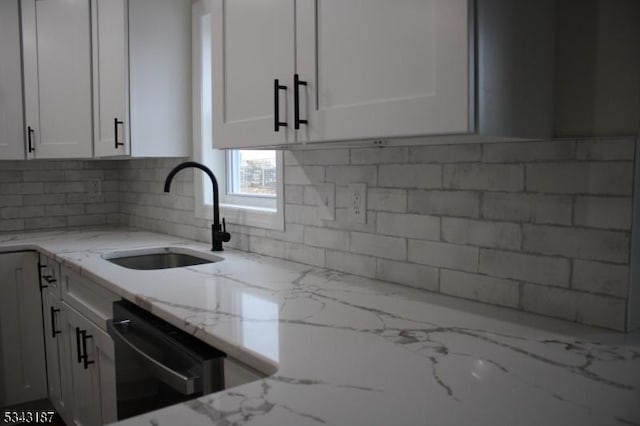 kitchen with white cabinets, black dishwasher, light stone countertops, and a sink