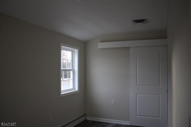 spare room with dark wood-type flooring, baseboards, visible vents, and a baseboard radiator