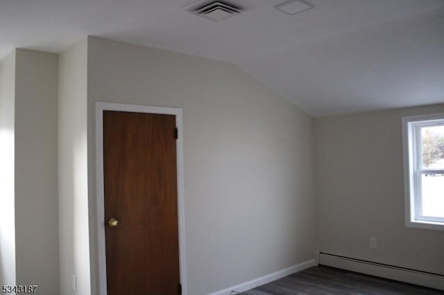 spare room featuring visible vents, lofted ceiling, a baseboard heating unit, dark wood-style floors, and baseboards