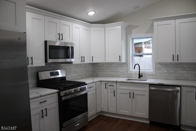 kitchen with light stone countertops, dark wood finished floors, a sink, appliances with stainless steel finishes, and white cabinetry