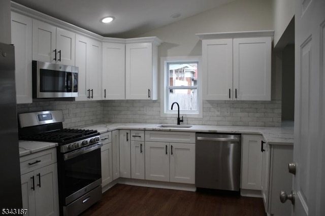 kitchen with light stone countertops, dark wood finished floors, a sink, stainless steel appliances, and white cabinetry