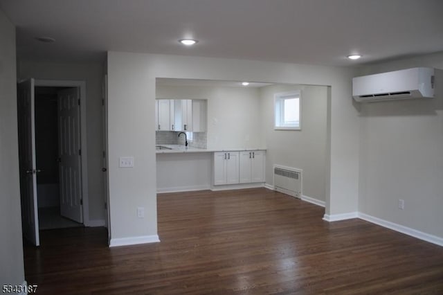 below grade area featuring dark wood finished floors, radiator heating unit, a wall unit AC, recessed lighting, and baseboards