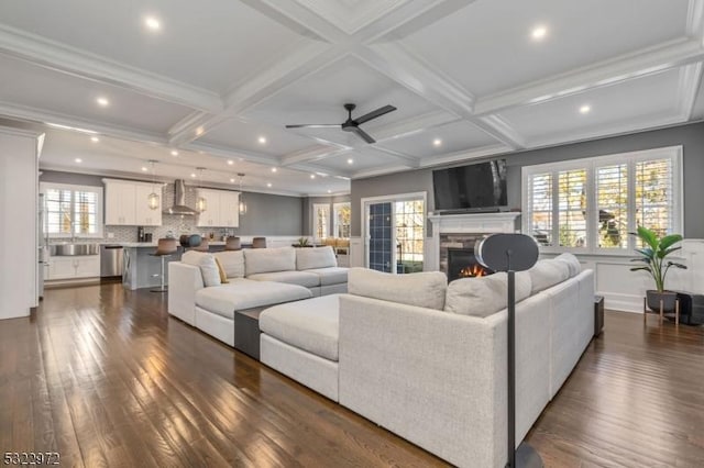 living room with beam ceiling, coffered ceiling, a lit fireplace, and ceiling fan