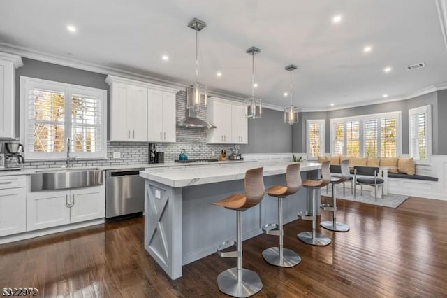 kitchen featuring visible vents, a center island, stainless steel dishwasher, wall chimney exhaust hood, and a sink