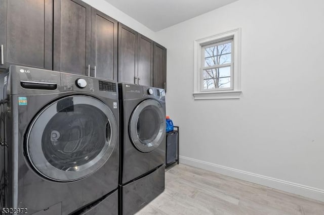 clothes washing area featuring cabinet space, washing machine and dryer, baseboards, and light wood finished floors