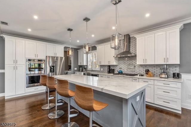 kitchen with a center island, stainless steel appliances, a breakfast bar area, wall chimney range hood, and decorative backsplash