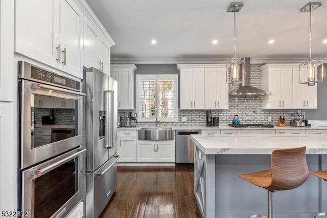 kitchen featuring a sink, white cabinetry, stainless steel appliances, a breakfast bar area, and wall chimney range hood