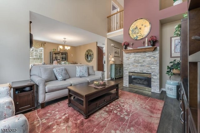 living room featuring a towering ceiling, a fireplace, an inviting chandelier, and wood finished floors