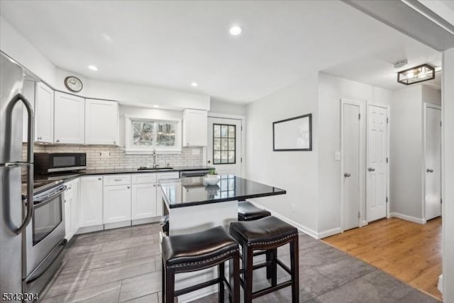 kitchen with dark countertops, a breakfast bar, decorative backsplash, appliances with stainless steel finishes, and white cabinets