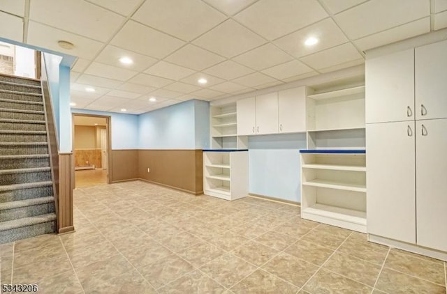 finished basement with recessed lighting, a drop ceiling, wainscoting, and stairs