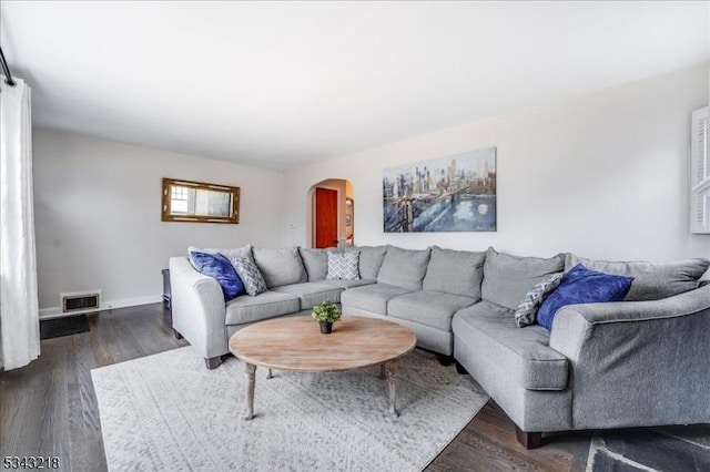 living area featuring dark wood-style floors, arched walkways, visible vents, and baseboards