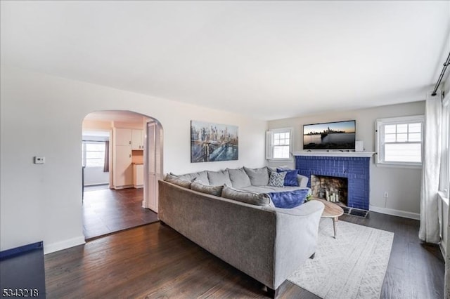 living room featuring arched walkways, a brick fireplace, and a wealth of natural light