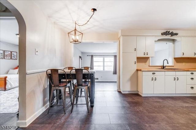 kitchen featuring white cabinetry, decorative light fixtures, arched walkways, and a sink