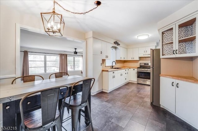 kitchen with under cabinet range hood, gas range, white cabinetry, and a sink