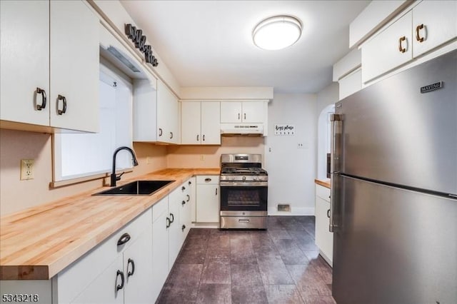 kitchen with wooden counters, a sink, stainless steel appliances, under cabinet range hood, and white cabinetry