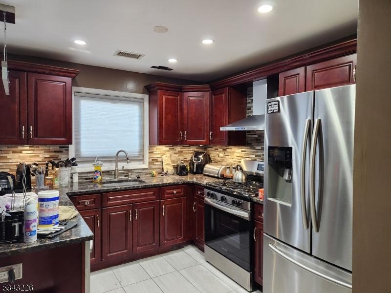 kitchen with visible vents, a sink, dark brown cabinets, appliances with stainless steel finishes, and wall chimney exhaust hood