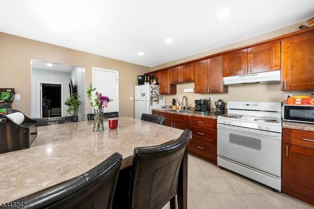 kitchen with under cabinet range hood, a breakfast bar, light tile patterned floors, white appliances, and a sink