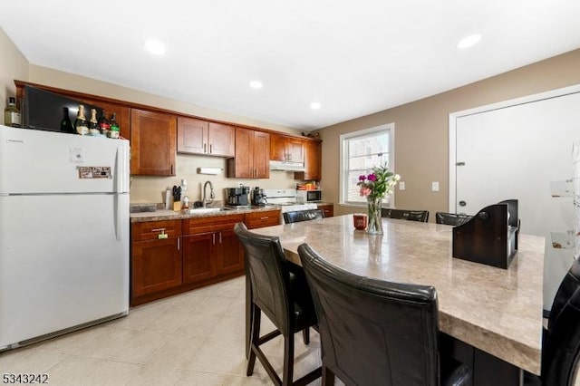 kitchen featuring under cabinet range hood, a kitchen bar, range, freestanding refrigerator, and a sink