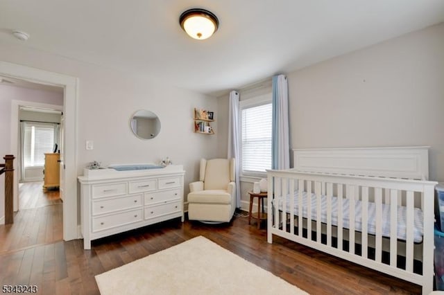 bedroom with multiple windows, a crib, and dark wood-type flooring