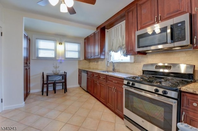 kitchen featuring a ceiling fan, a sink, light stone counters, appliances with stainless steel finishes, and decorative backsplash