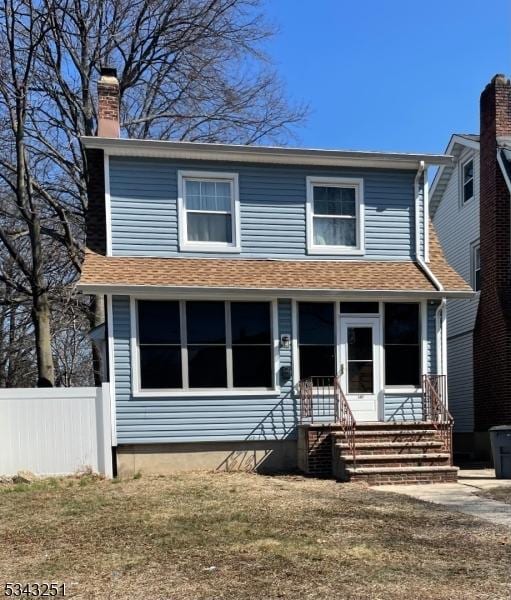 view of front of home with fence, entry steps, roof with shingles, a chimney, and a sunroom