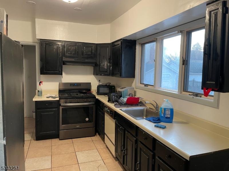 kitchen featuring a sink, under cabinet range hood, gas range, freestanding refrigerator, and dark cabinets