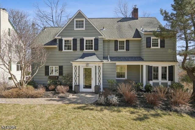 view of front of house featuring a front yard, a chimney, and a shingled roof