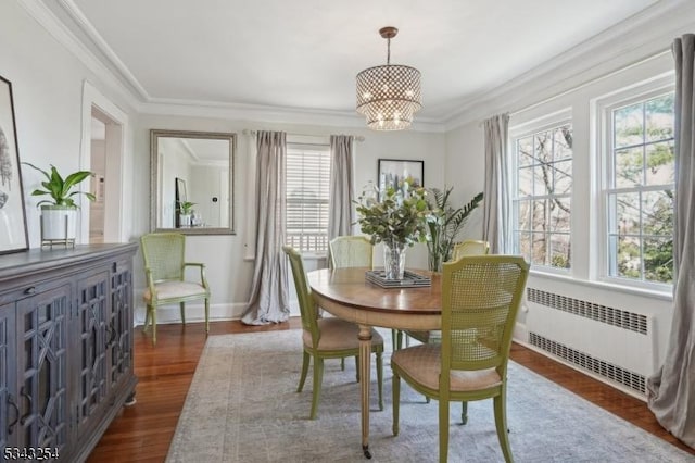 dining room featuring radiator, baseboards, dark wood finished floors, ornamental molding, and an inviting chandelier