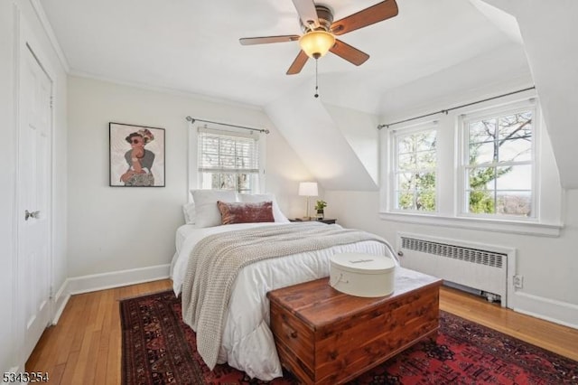 bedroom with light wood-type flooring, baseboards, radiator, and lofted ceiling