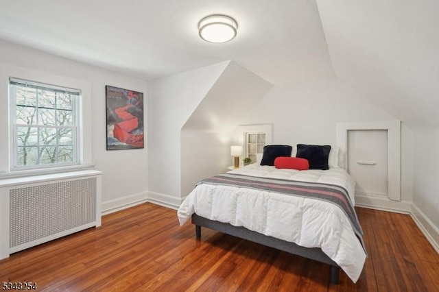 bedroom with vaulted ceiling, radiator, baseboards, and wood-type flooring