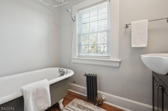 bathroom with vanity, radiator, wood finished floors, baseboards, and a soaking tub