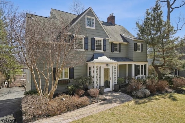 view of front facade with a chimney, a front lawn, and roof with shingles