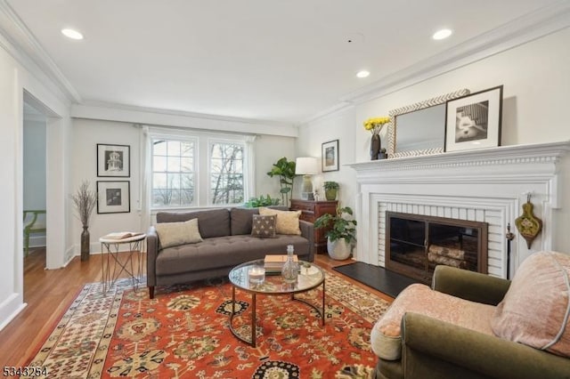 living area featuring a glass covered fireplace, recessed lighting, wood finished floors, and crown molding