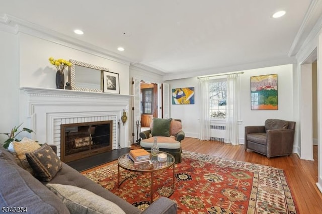 living area featuring a glass covered fireplace, radiator, wood finished floors, and ornamental molding