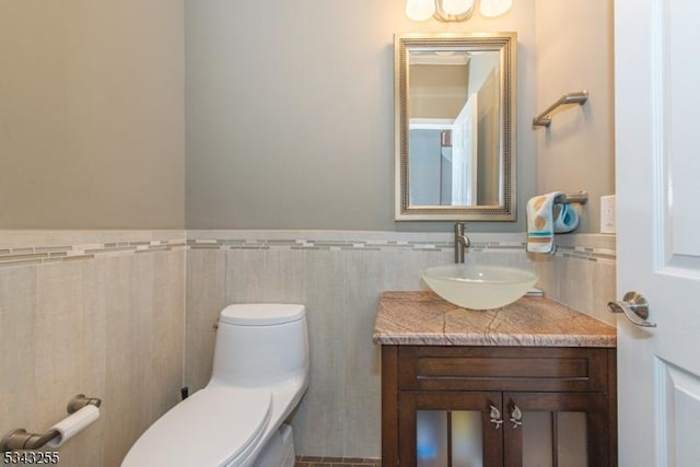 half bathroom with a wainscoted wall, toilet, tile walls, and vanity