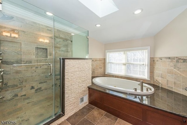 full bathroom featuring a garden tub, a stall shower, recessed lighting, vaulted ceiling with skylight, and tile walls