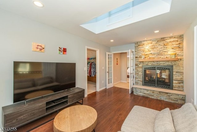 living area featuring wood finished floors, baseboards, a skylight, recessed lighting, and a stone fireplace