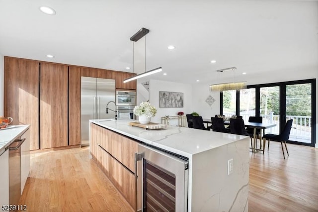 kitchen with light wood-style flooring, modern cabinets, beverage cooler, and appliances with stainless steel finishes