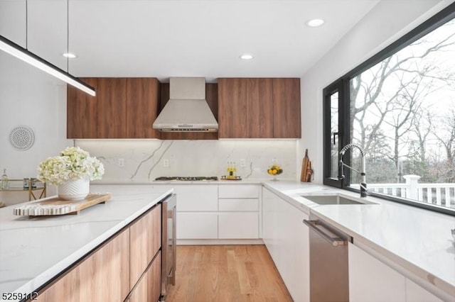 kitchen featuring a sink, light countertops, stainless steel dishwasher, wall chimney exhaust hood, and modern cabinets