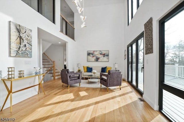 living room with wood finished floors, visible vents, an inviting chandelier, stairs, and a towering ceiling