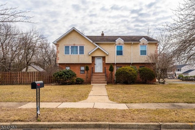 bi-level home with brick siding, stucco siding, a front lawn, and fence