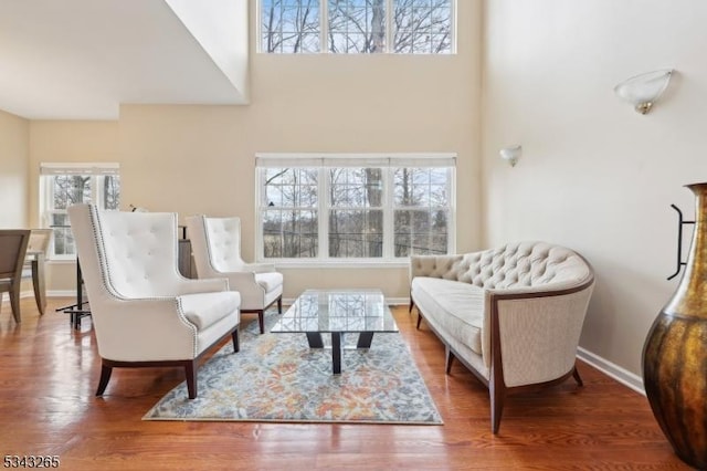 living area with a towering ceiling, baseboards, and wood finished floors