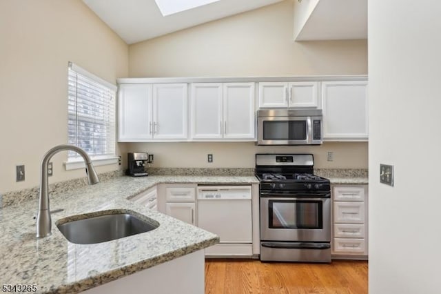 kitchen with light stone counters, stainless steel appliances, light wood-style floors, white cabinetry, and a sink