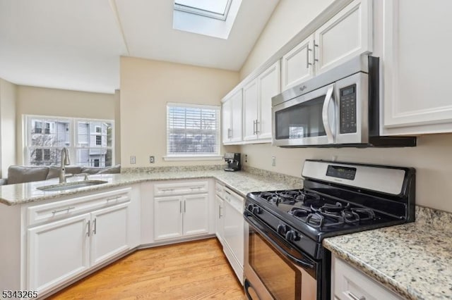 kitchen with white cabinets, appliances with stainless steel finishes, a skylight, and a sink