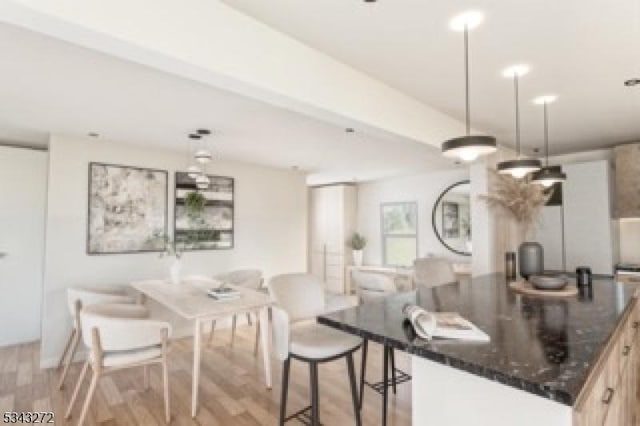 kitchen featuring pendant lighting, light wood-style flooring, a breakfast bar, a center island, and dark stone counters