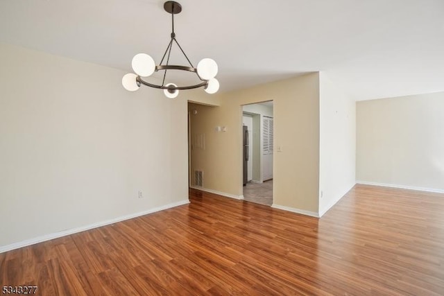 spare room with baseboards, a notable chandelier, and wood finished floors